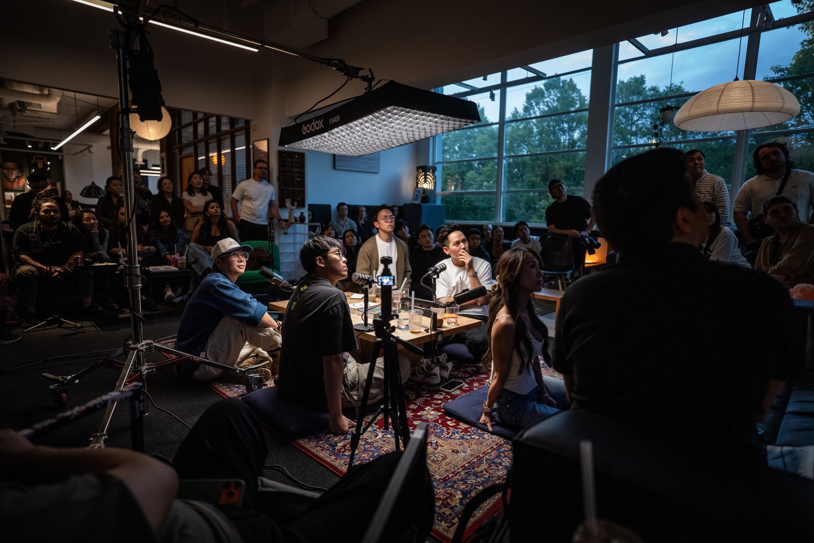 The panel on floor cushions under the softbox, with the crowd and the window wall behind